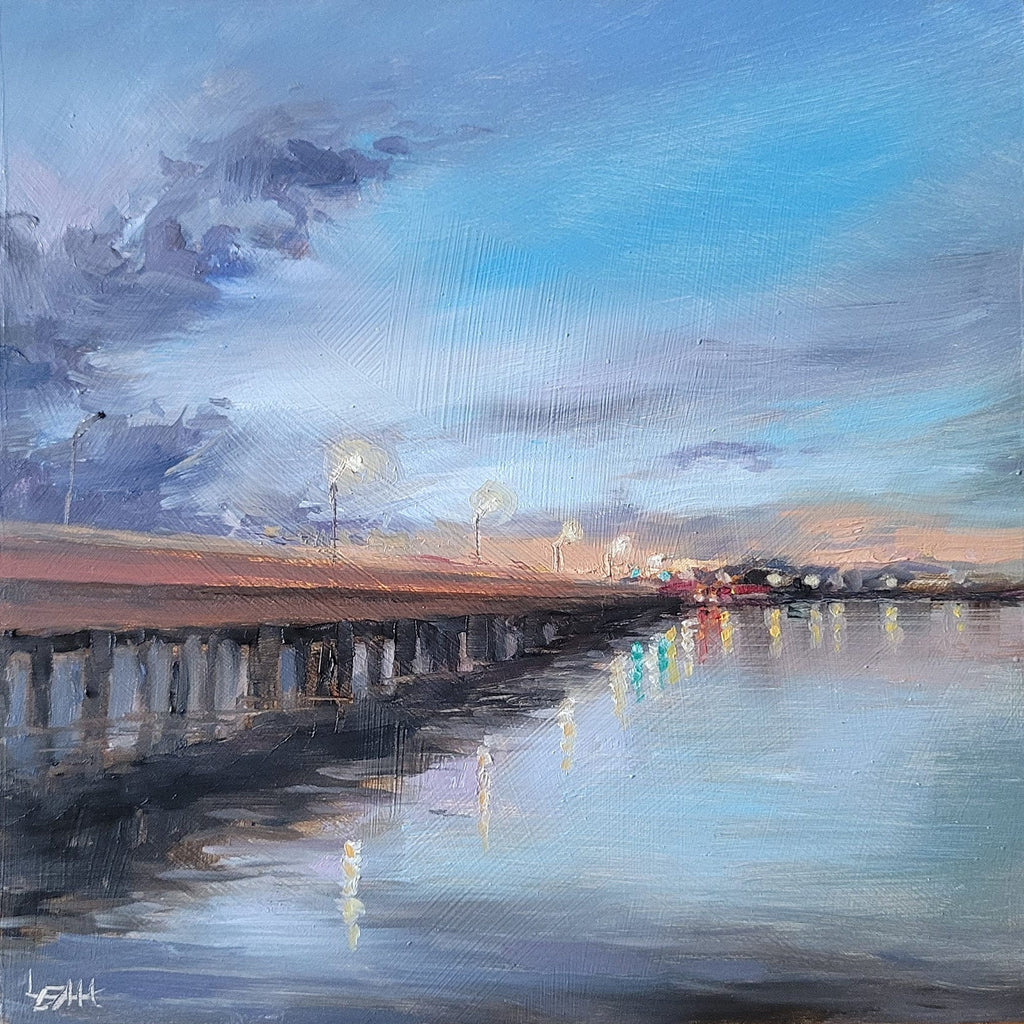 A square canvas painting of a pier extending over calm water under a blue and gray sky, with warm sunset light and reflections, displayed on a wooden surface.