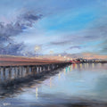A square canvas painting of a pier extending over calm water under a blue and gray sky, with warm sunset light and reflections, displayed on a wooden surface.